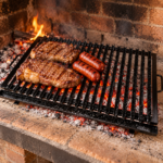 Emparrillado de hierro ángulo enlozado con grasera, carne y chorizos sobre brasas en una parrilla argentina.